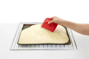 Close-up of flexible red silicone baking scraper smoothing batter on a tray surface