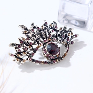 Detailed close-up of antique silver Evil Eye brooch with colorful crystals on white background