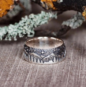 Close-up of vintage silver ring with engraved mountain and forest relief on linen