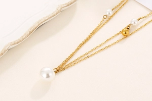 Detail of a gold double-layer necklace featuring white pearls on a soft beige background
