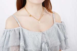 Detailed view of layered gold necklace with pearls on a model wearing an off-shoulder top