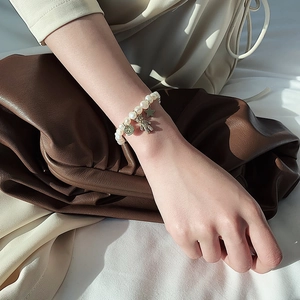 Baroque pearl bracelet with pink bear and gold charms worn on a woman's wrist