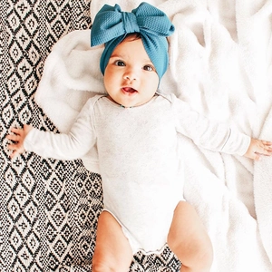 Detail of baby girl wearing a large blue waffle fabric bow headband on a soft white rug