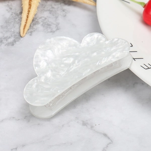 Macro shot of cloud-shaped white acetate hair claw with pearlescent texture on marble