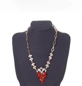 Close-up of a red gemstone flower necklace displayed on a dark grey velvet neck bust