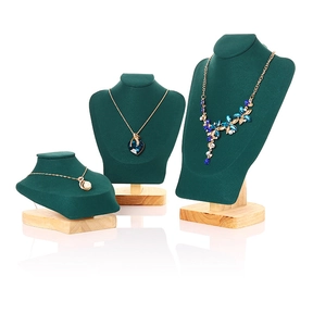 Three dark green velvet necklace busts on wooden bases in tiered sizes with reflections