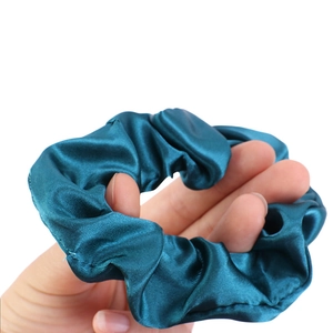 Detail of a dark teal satin scrunchie showing glossy fabric texture and elastic stretch