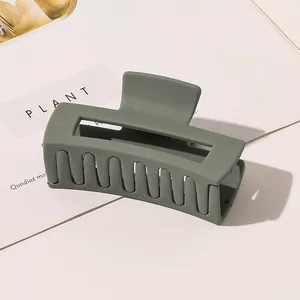 Close-up of a large matte green square hair claw clip on a stylish white book background