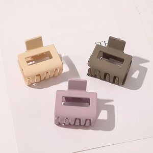 Three matte rectangular hair claws in cream, sage green, and dusty pink on a magazine