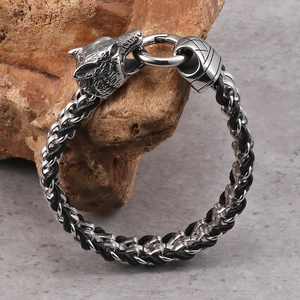 Silver wolf head buckle bracelet with black braided leather on rustic stone
