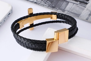 Detailed side view of black woven leather bracelet with a polished gold cross and magnetic clasp