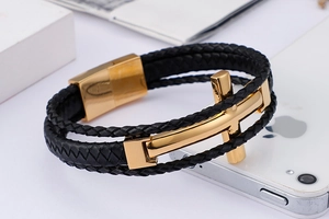 Macro shot of men's triple-layer black leather braided bracelet with gold cross detail