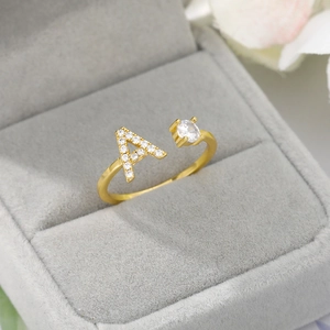 Adjustable gold ring with letter A pendant and white zircon stones in a gray jewelry box