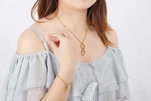 Detail of gold infinity symbol necklace and bracelet set with small heart charm on model