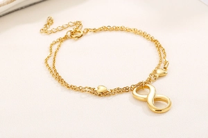 Detail of gold layered bracelet with heart charms and infinity symbol on fabric