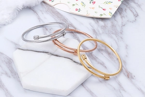 Three-piece stack of twisted cable bangles in silver, gold, and rose gold on marble