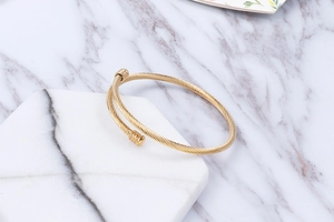 Detail of a twisted rope gold bangle displayed on white hexagonal marble stones