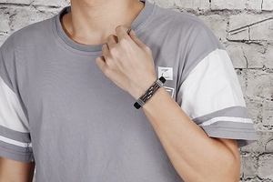 Detailed view of men's black braided leather bracelet with industrial steel charms on wrist