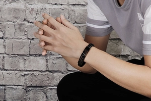 Detail of men's black braided leather bracelet with matte metal clasp on male wrist