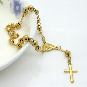 Bracciale rosario dorato con ciondolo a croce esposto su un piatto di ceramica