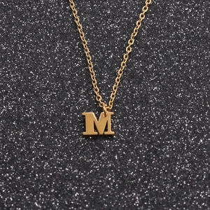 Golden stainless steel letter M pendant necklace displayed on a black glitter background