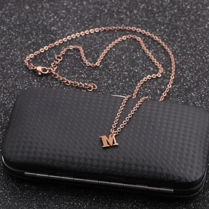 Detailed close-up of rose gold letter M necklace on black quilted jewelry box