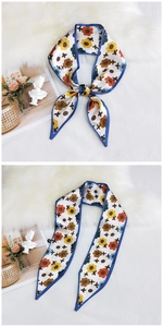 Detail of a floral print silk scarf with navy blue edges shown on a fuzzy white texture