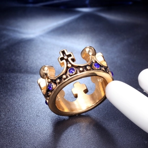 Macro detail of golden crown ring featuring blue gemstones on a black textured surface