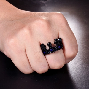 Close-up of a black crown ring with blue gems worn on a finger over dark reflection