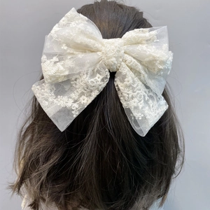 Close-up of a large white lace bow hair clip with floral embroidery on a hair model