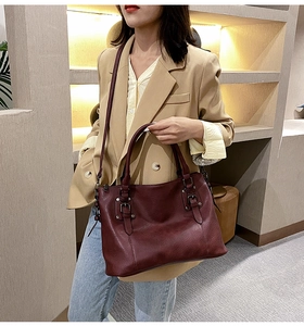 Detail of burgundy lychee grain leather handbag with metal buckle and reinforced handle