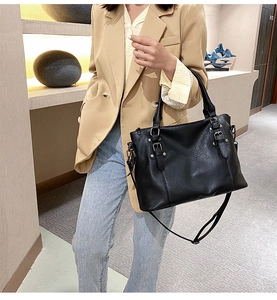 Chic black textured tote bag with metal buckle shown on a model in a minimalist suit