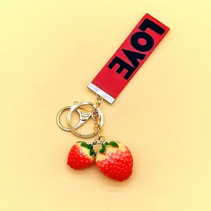 Close-up of red LOVE ribbon keychain with strawberry charms and golden hardware