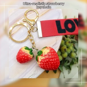 Macro detail of realistic resin strawberry pendant with LOVE ribbon and gold keychain