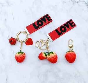 Cute strawberry keychains with red LOVE ribbons and golden bells on marble background