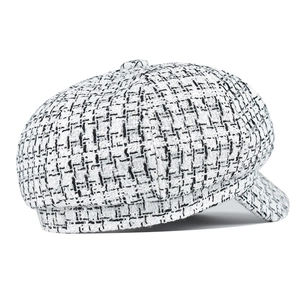 Detail of black and white tweed newsboy cap showing refined plaid texture and stiff brim