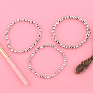 Vue détaillée d'un ensemble de trois bracelets de perles argentées sur fond rose vif