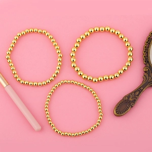 Detalle de tres pulseras de bolas doradas pulidas sobre un fondo rosa de tocador