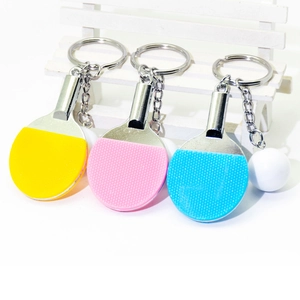 Miniature table tennis racket keychains in yellow, pink, and blue on a white bench