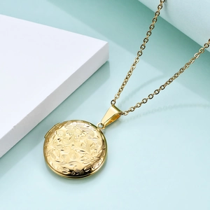 Detail of a vintage golden round locket necklace with floral relief and O-chain