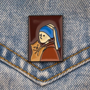 Gros plan d'un badge émaillé La Jeune Fille à la Perle avec un chat sur du denim