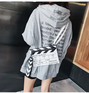 Detail view of white movie clapperboard crossbody bag on a grey hoodie streetwear style