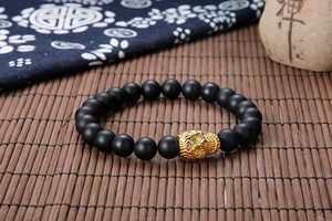 Detail view of tiger eye beaded bracelet with gold skull charm on a bamboo mat