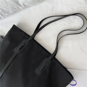 Close-up of reinforced shoulder strap stitching and nylon texture on black tote bag