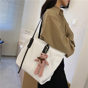 Side view of white large capacity tote bag with black straps and pink bear charm