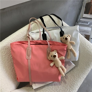 Detail of large nylon tote bags in pink and white featuring cute plush bear charms