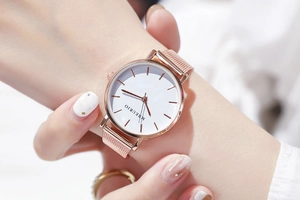 Close-up of a rose gold mesh band watch on wrist with a minimalist white dial
