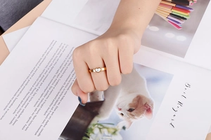 Detailed view of a gold heart ring with white shell inlay worn on a female hand