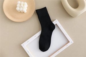 Close-up of black knit crew sock with ribbed cuffs on a minimalist warm-toned background