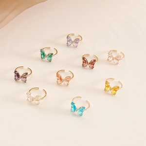 Top view of multiple colorful glass butterfly rings with adjustable gold-tone bands
